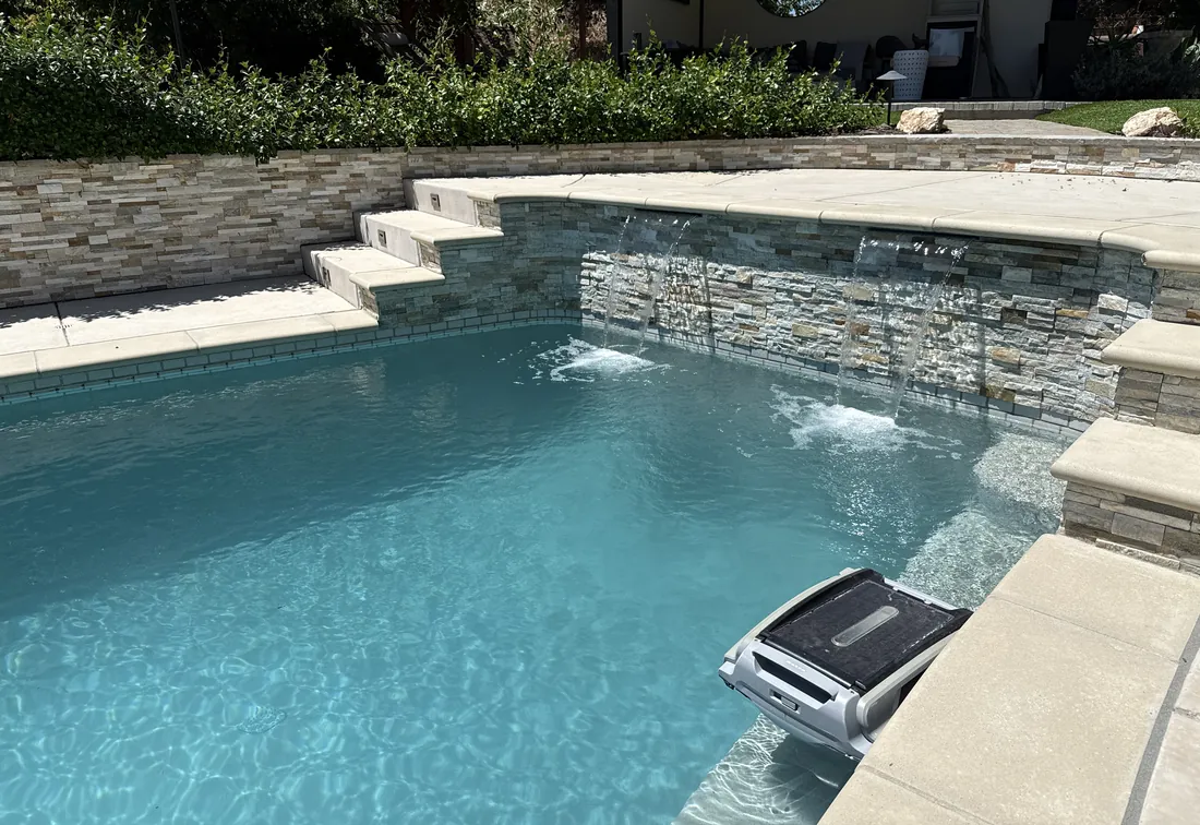 Clean Marin County pool with waterfall features and a robotic cleaner running during weekly service